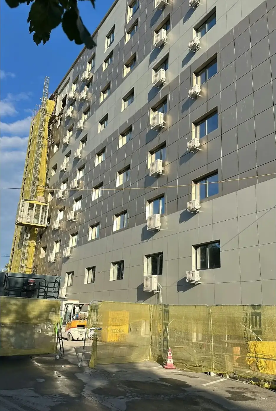 Fațada unui bloc înalt cu multe unități exterioare de aer condiționat montate sub ferestre, sub un cer albastru