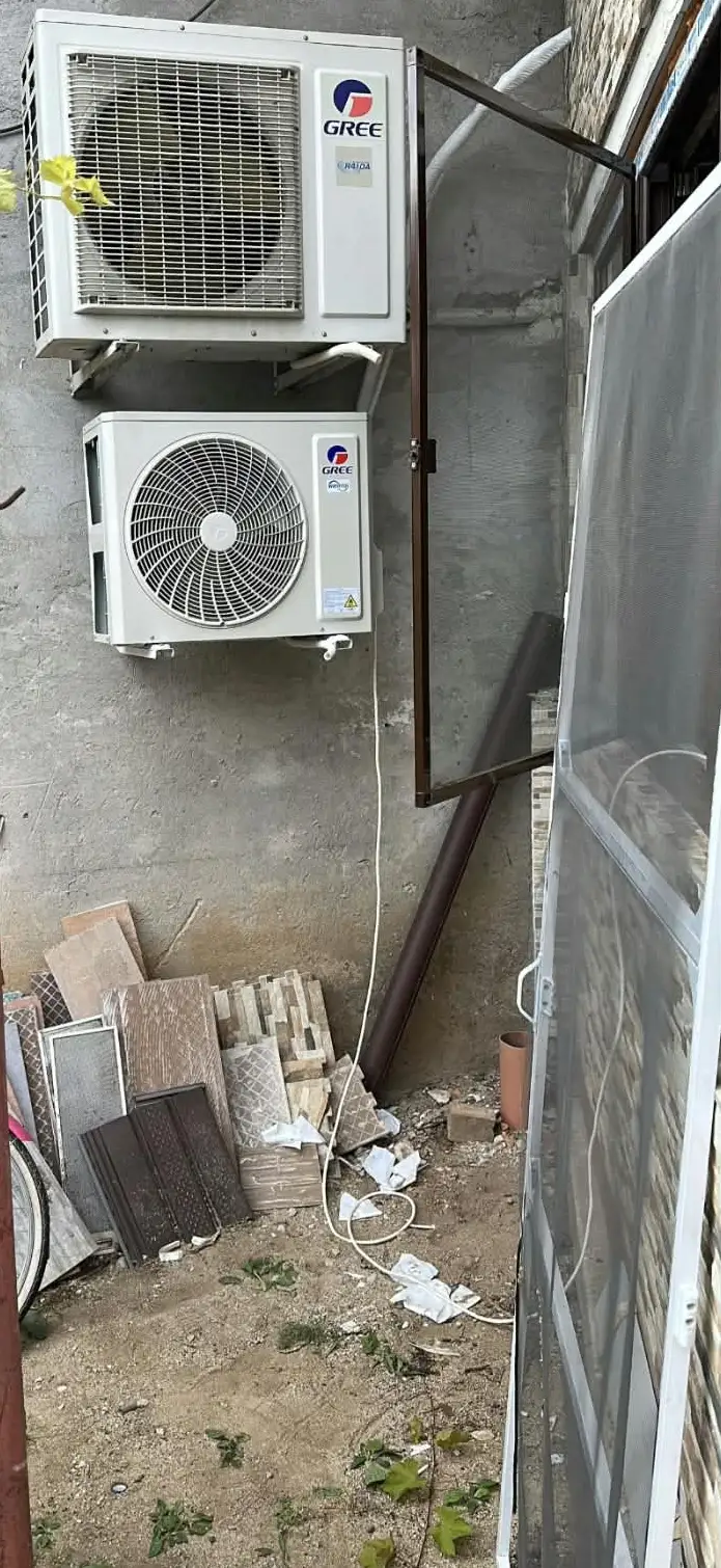 Două unități exterioare de aer condiționat Gree, una sub alta, pe console fixate într-un perete de beton, cu cablul coborât pe perete